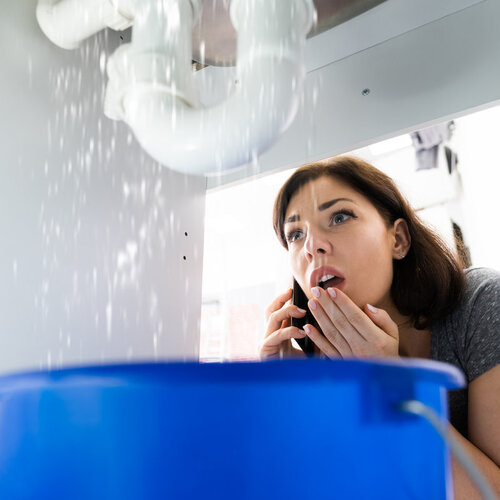 woman making a phone call while dealing with a plumbing emergency