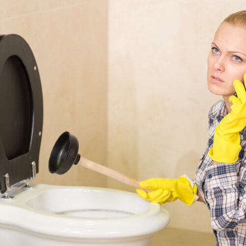 woman calling a plumber while plunging a toilet