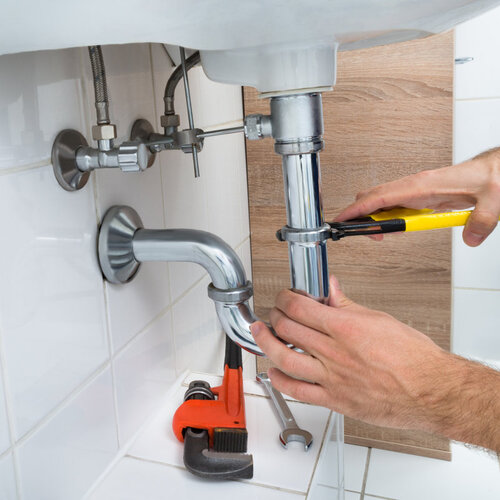 close-up of a plumber working on pipes under a sink